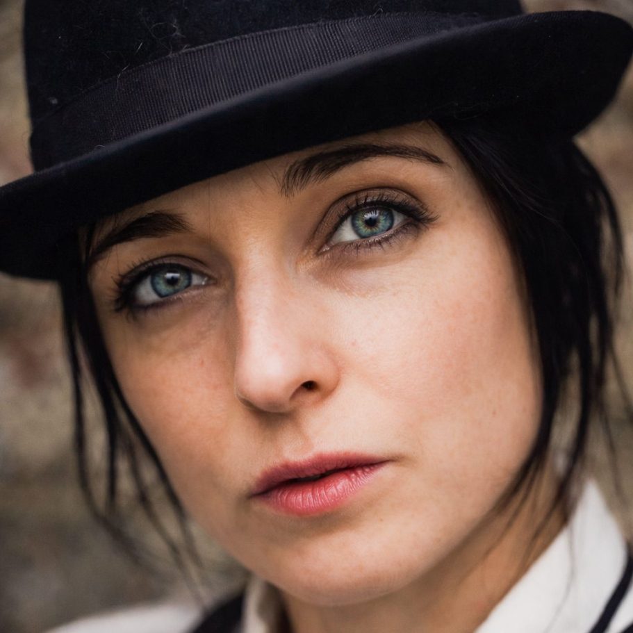 Porträt einer Frau mit Hut und intensiven blauen Augen vor einer neutralen Hintergrund.